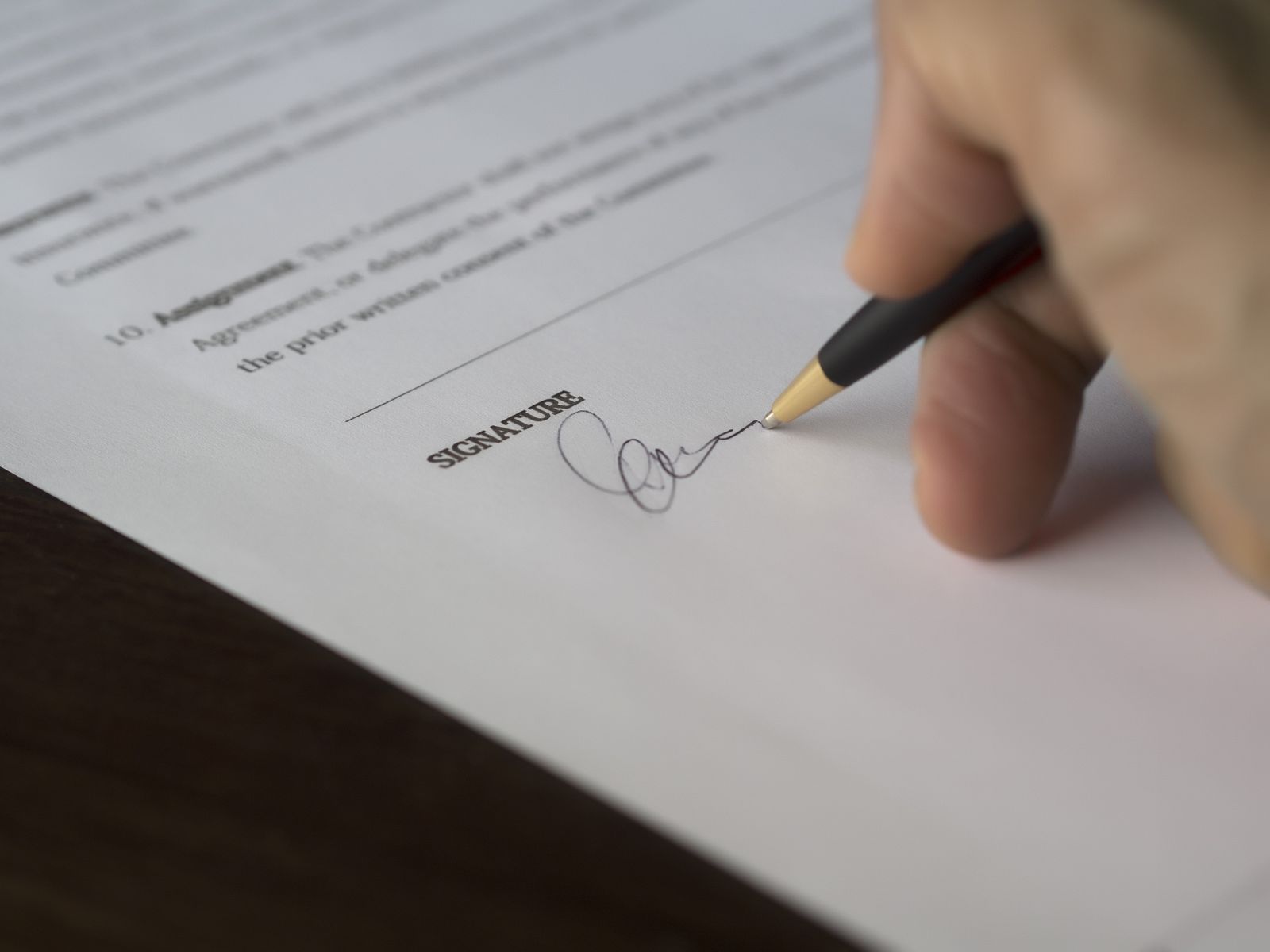 Mão assinando a última página de um contrato impresso